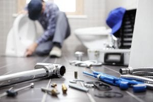 Closeup of tools on bathroom floor with plumber working in background