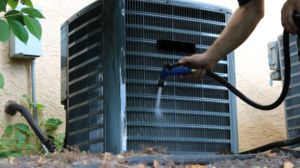Air conditioner repair person hosing down the outdoor unit 