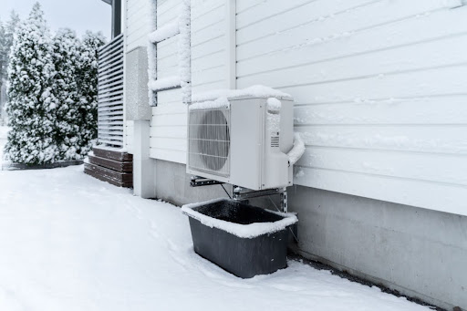 A heat pump outside a home in snow.